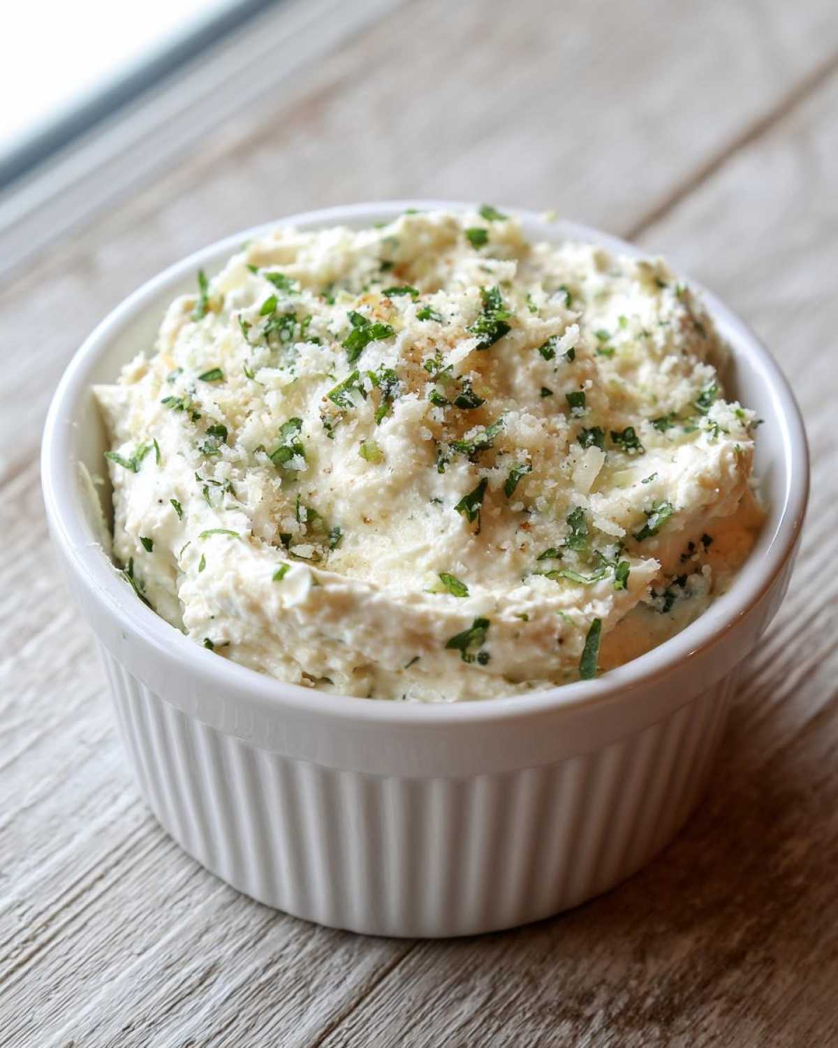 A close-up of thick, creamy Copycat Pizza Garlic Parmesan Dip Sauce topped with grated cheese and fresh parsley.