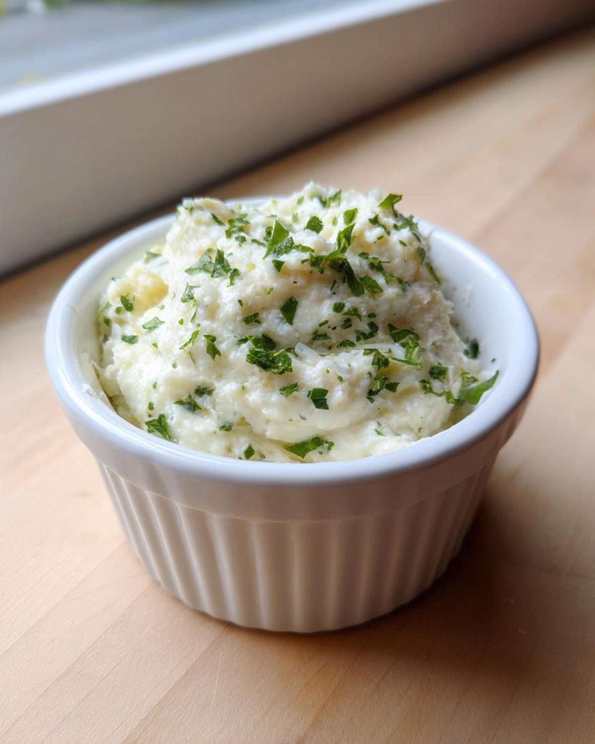 A small white ramekin filled with thick, creamy Copycat Pizza Garlic Parmesan Dip Sauce, topped with fresh chopped parsley.