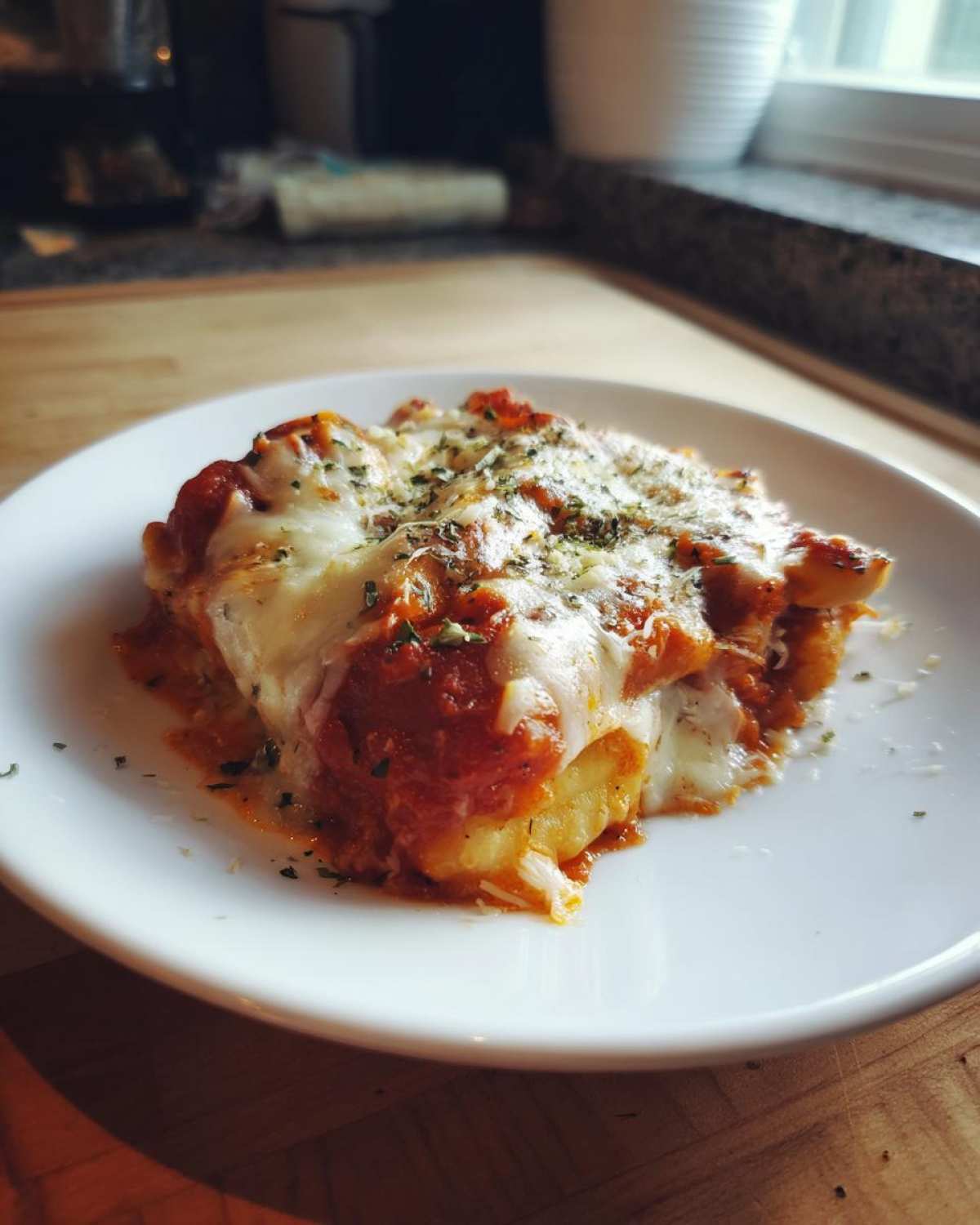 A close-up of a serving of Creamy Roasted Garlic Tomato Gnocchi Bake covered in melted cheese and herbs.