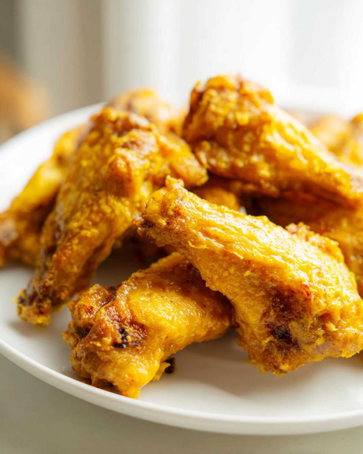 Close-up of crispy, golden chicken wings tossed in a rich Copycat Garlic Parmesan Wing Sauce on a white plate.
