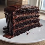 A tall, three-layer slice of Death by Chocolate Cake covered in rich, dripping chocolate ganache on a white plate.