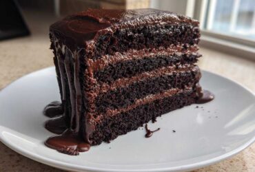 A tall, three-layer slice of Death by Chocolate Cake covered in rich, dripping chocolate ganache on a white plate.
