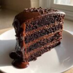 A decadent slice of 3 layer Death by Chocolate Cake covered in rich chocolate ganache dripping down the side.
