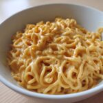 Close-up of ramen noodles generously coated in a creamy, orange-hued Easy 5-Minute Peanut Sauce with visible chili flakes.