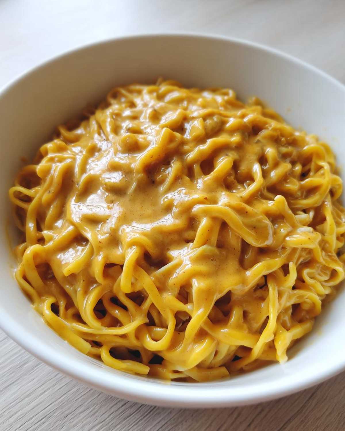 Close-up of noodles generously coated in a creamy, orange-hued Easy 5-Minute Peanut Sauce in a white bowl.