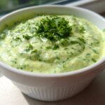 A close-up of the Easy 5-Minute Salsa Verde Yogurt Dip, a creamy light green dip topped with fresh parsley, served in a white ramekin.