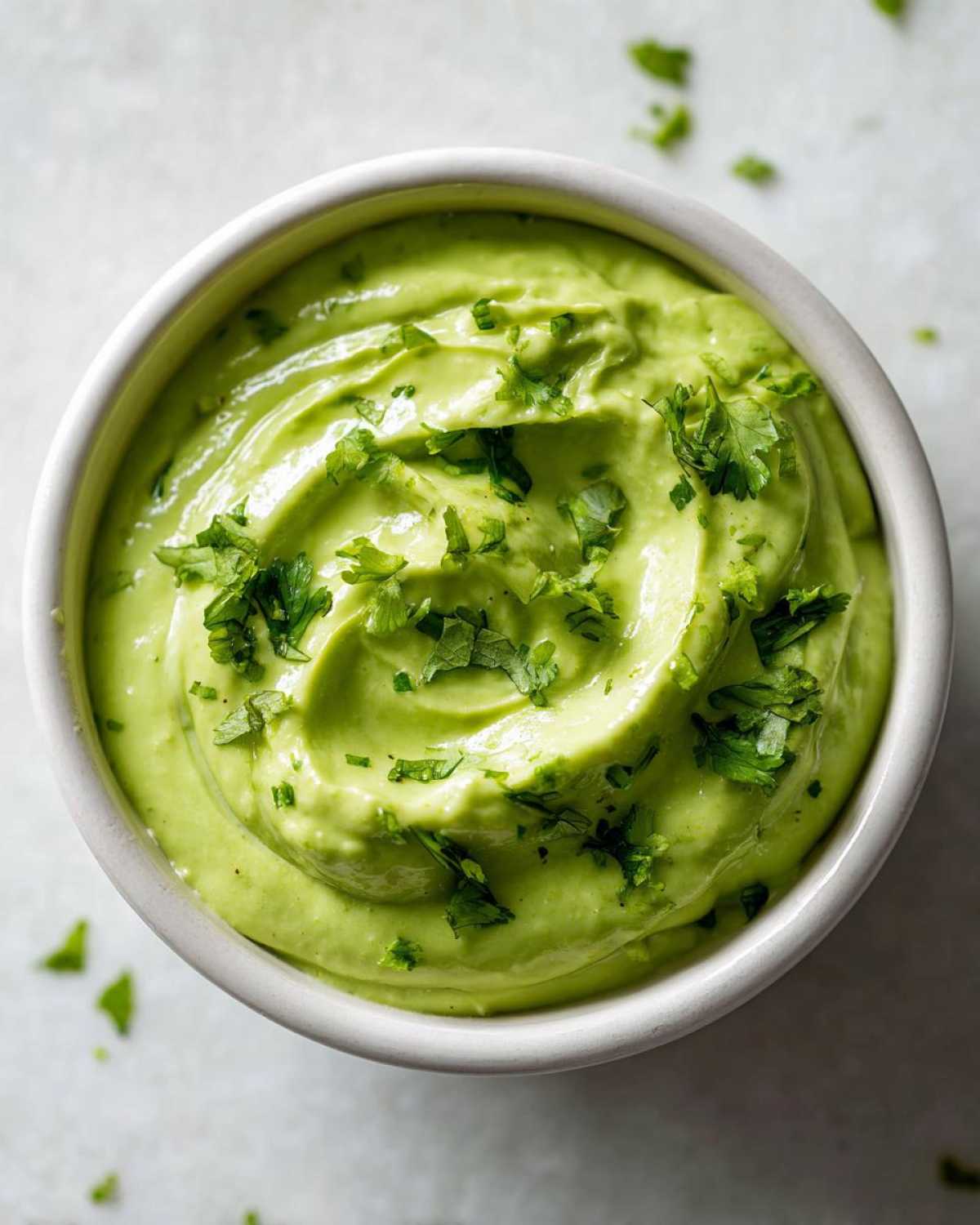 Overhead shot of a small white bowl filled with creamy green Easy 5-Minute Salsa Verde Yogurt Dip, topped with fresh cilantro.