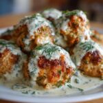 Close-up of golden brown Easy Creamy Greek Chicken Meatballs smothered in a white dill sauce.