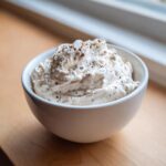 A close-up of thick Easy Greek Yogurt Caesar Dressing, topped with coarse salt and pepper, in a white bowl.