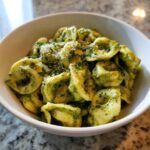 Close-up of a white bowl filled with Easy One-Pot Creamy Pesto Tortellini topped with grated cheese.
