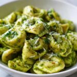 A close-up of a white bowl filled with Easy One-Pot Creamy Pesto Tortellini, topped with grated Parmesan cheese.