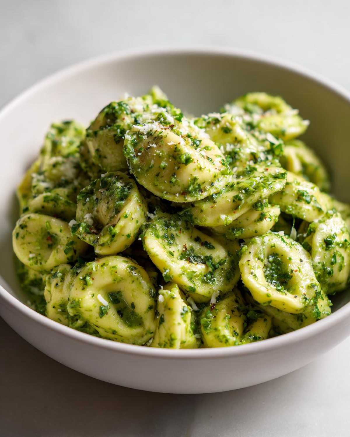 A close-up shot of a white bowl filled with Easy One-Pot Creamy Pesto Tortellini topped with grated Parmesan cheese.