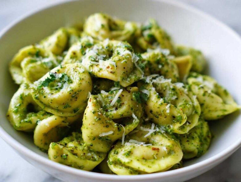 A close-up of a white bowl filled with Easy One-Pot Creamy Pesto Tortellini, topped with grated Parmesan cheese.