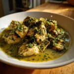 Close-up of chunks of chicken coated in a vibrant green, creamy salsa verde sauce, served in a white bowl.