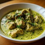 Close-up of tender chicken pieces coated in a vibrant, creamy salsa verde sauce, garnished with fresh herbs.