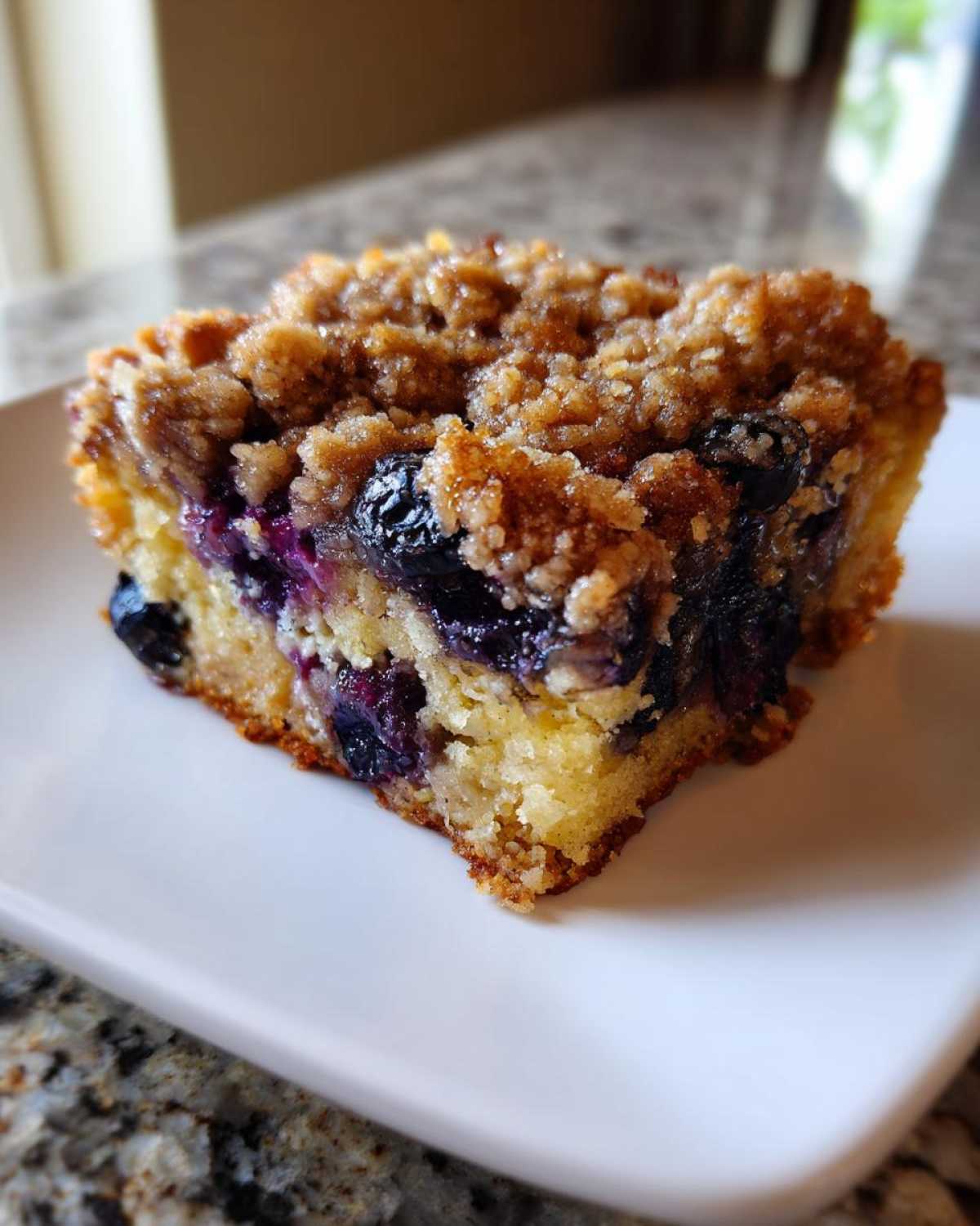 Close-up of a square slice of Easy Sheet Pan Blueberry Streusel Pancake showing moist cake, blueberries, and crumb topping.