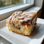 A close-up of a square slice of Easy Sheet Pan Cinnamon Roll Pancake Bake drizzled with white icing.