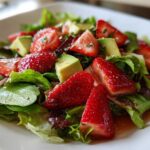 Close-up of a fresh Easy Strawberry Avocado Salad featuring bright red strawberries, green avocado chunks, and mixed greens tossed in vinaigrette.