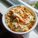 Close-up of a creamy, orange-hued Garden Vegetable Spread mixed with shredded carrots and green herbs in a white bowl.