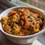 A white bowl filled with a chunky, orange-hued Garden Vegetable Spread mixed with visible green herbs and red tomato pieces.