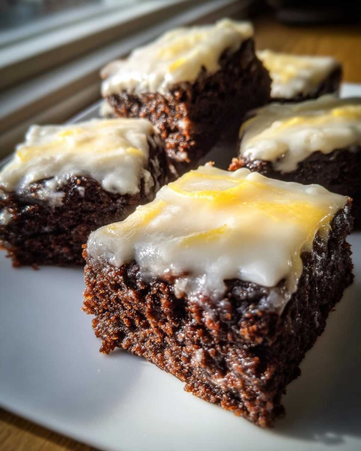 Close-up of rich, dark Gingerbread Bars with Zesty Lemon Glaze squares arranged on a white plate.