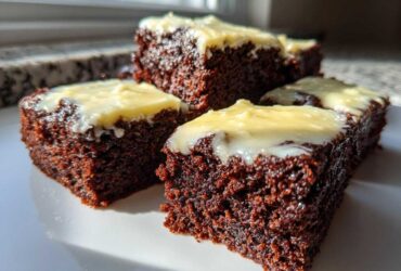 Four rich, dark squares of Gingerbread Bars with Zesty Lemon Glaze stacked on a white plate.
