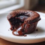 Close-up of a single Gluten-Free Chocolate Lava Brownie Cup with molten chocolate oozing out onto a white plate.