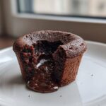 A single Gluten-Free Chocolate Lava Brownie Cup with molten chocolate oozing out onto a white plate.