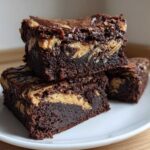 Three fudgy Gluten-Free Chocolate Peanut Butter Swirl Brownies stacked on a white plate.