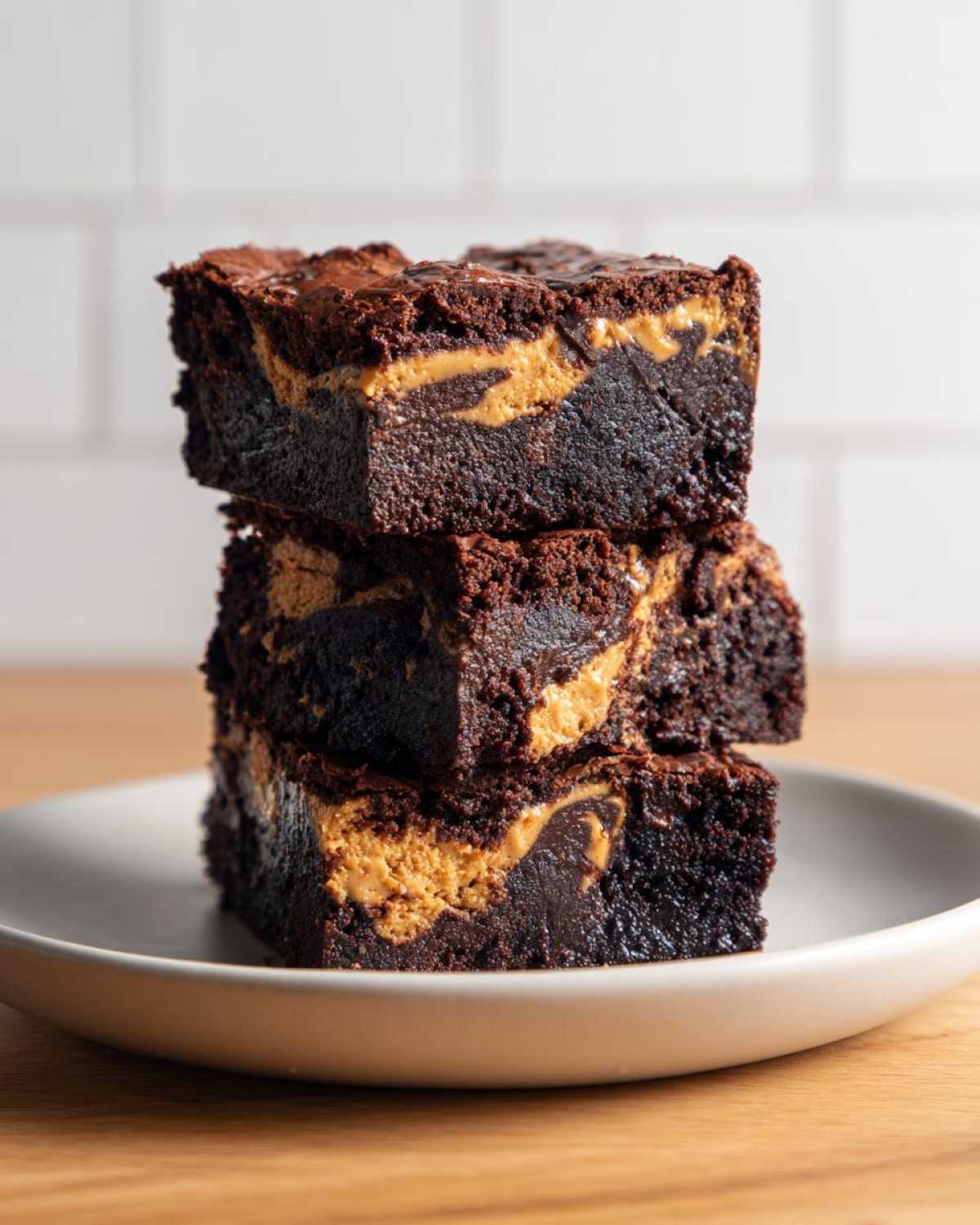 A stack of three fudgy Gluten-Free Chocolate Peanut Butter Swirl Brownies on a light plate.