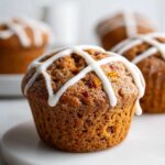 A close-up of a single Gluten-Free Hot Cross Bun Muffin topped with white icing in a cross pattern.