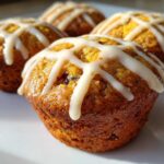 Close-up of four golden brown Gluten-Free Hot Cross Bun Muffins topped with white cross icing on a white plate.