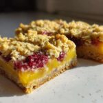 Two slices of Gluten-Free Lemon Berry Crumble Bars showing the bright yellow lemon layer and raspberry topping.