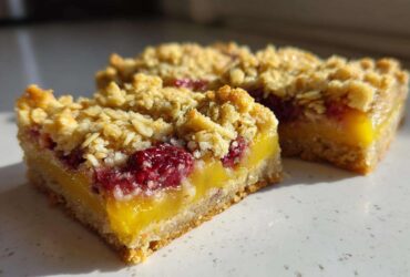 Two slices of Gluten-Free Lemon Berry Crumble Bars showing the bright yellow lemon layer and raspberry topping.