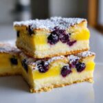 Two stacked squares of Gluten-Free Lemon Blueberry Layer Bars topped with powdered sugar and visible blueberries.