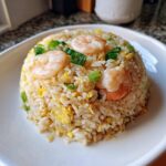 A perfectly molded serving of Gluten-Free Lemon Pepper Fried Rice topped with shrimp and green onions.