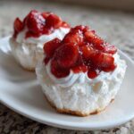 Close-up of two Gluten-Free Lemon Strawberry Angel Food Cups topped with whipped cream and macerated strawberries.