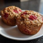 Two perfectly baked Gluten-Free Strawberry Oat Muffins topped with visible oats and bright red strawberry pieces.
