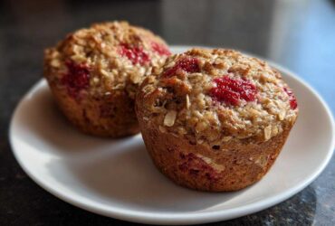 Two perfectly baked Gluten-Free Strawberry Oat Muffins topped with visible oats and bright red strawberry pieces.