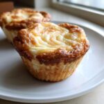 Close-up of two freshly baked Cheesecake Muffins with golden brown edges and swirled creamy tops.