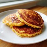 A stack of three golden brown, perfectly cooked Cornmeal Pancakes served on a white plate.