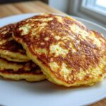 A stack of three perfectly cooked, golden brown Cornmeal Pancakes served on a white plate.
