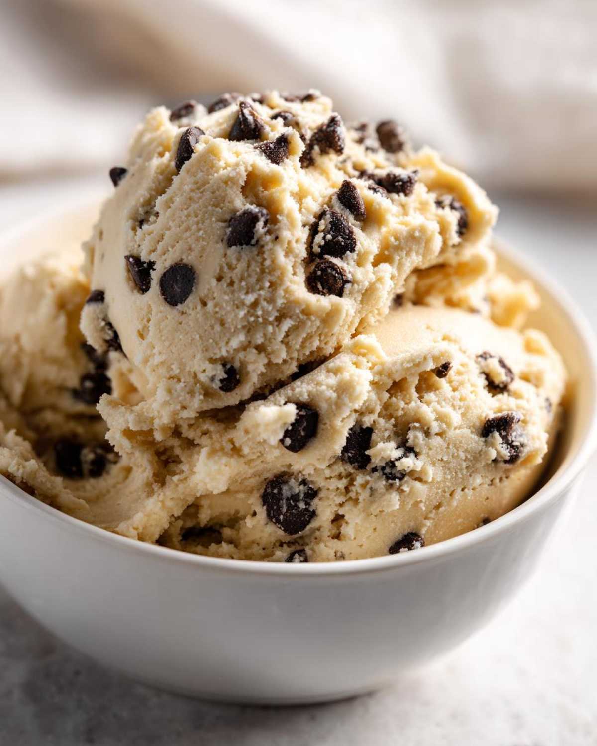 Close-up of scoops of creamy Greek Yogurt Cookie Dough loaded with mini chocolate chips in a white bowl.