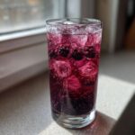 A tall glass filled with vibrant, bubbly Iced Blackberry Sage Tea, ice cubes, and whole blackberries.