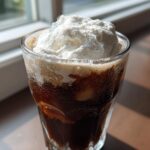 A refreshing glass of Iced Coconut Mocha with Cold Foam piled high on top, showing condensation on the glass.