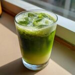 A tall glass filled with a vibrant green Iced Matcha Pineapple Refresher, layered over a lighter base and topped with ice cubes.