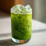 A tall glass filled with a bright green Iced Matcha Pineapple Refresher topped with large ice cubes.