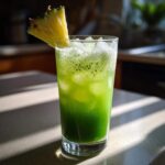 A tall glass filled with a vibrant green Iced Pineapple Matcha Spritz, filled with ice and garnished with a pineapple wedge.