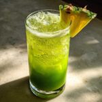 A refreshing Iced Pineapple Matcha Spritz, bright green and bubbly, served over ice with a fresh pineapple wedge garnish.