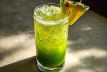 A refreshing Iced Pineapple Matcha Spritz, bright green and bubbly, served over ice with a fresh pineapple wedge garnish.